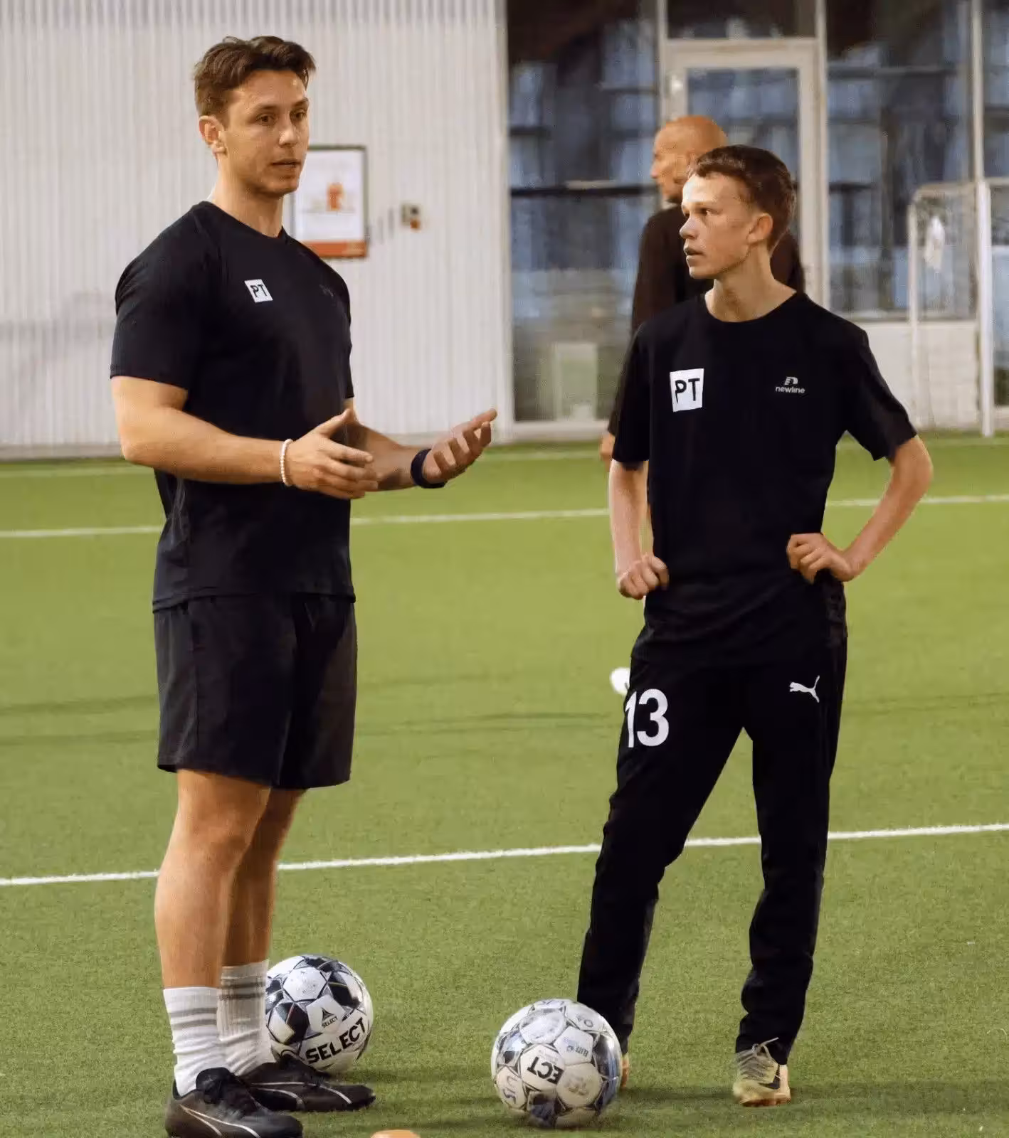 fysisk træner står med ung fodboldspiller under fysisk træning på fodboldbane